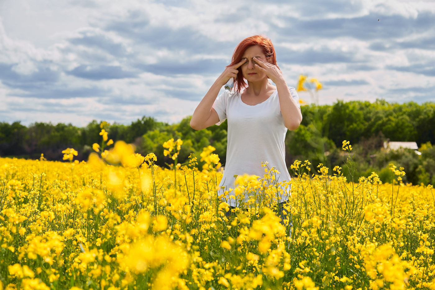 girl rubbing her eyes in field of flowers due to allergies